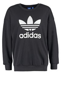 Černá mikina s dlouhými rukávy, žebrovanými manžetami a lemem. Má výrazné bílé logo Adidas a tři horizontální pruhy na vzoru listu.