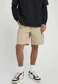 Shorts cargo couleur kaki avec deux poches latérales et une coupe droite, assortis à un t-shirt noir oversized et des baskets blanches de sport.