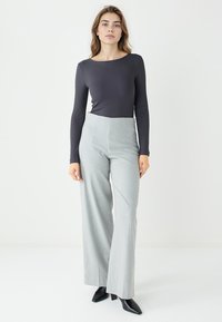 Langärmliges, geripptes dunkelgraues Oberteil kombiniert mit hochtaillierter, weit geschnittener hellgrauer Hose. Schwarze spitze Absätze runden das Outfit ab.