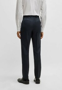 Pantaloni navy a righe sottili con vestibilità su misura, dotati di una texture liscia, tasche laterali e passanti per la cintura, abbinati a scarpe in pelle nera.