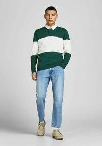 Camisa polo a rayas verdes y blancas con cuello abotonado, combinada con jeans rectos de color azul claro y zapatos beiges.