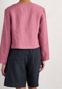 Rosa kort jacka av lätt tyg, med långa ärmar, rak skärning och subtil textur. Kombinerad med mörka shorts.