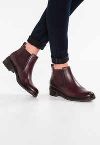 Burgundin nahka nilkkakengät, joissa on joustavat sivupaneelit, pyöristetty kärki ja pinoheijastin; käytetään taitettuina tummien farkkujen kanssa.