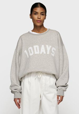 Grijze oversized sweatshirt met witte "10DAYS" tekst, ronde hals, ribgebreide manchetten en een zachte, textuurachtige stof. Draagt over witte broek.