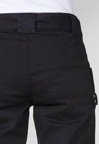 Pantalones negros con una textura suave, que presentan una cintura ajustada, un cierre de botón y detalles de bolsillos laterales. Diseño simple sin patrones visibles.