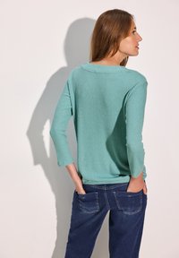 Mintgrön ribbad lång ärmad tröja med vid halsringning, kombinerad med mörkblå denimbyxor med bakfickor och lätt blekning.