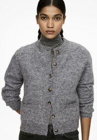 Grauer Wollcardigan mit Rundhalsausschnitt, Knopfverschluss und zwei Fronttaschen. Verfügt über gerippte Bündchen und eine strukturierte Oberfläche.