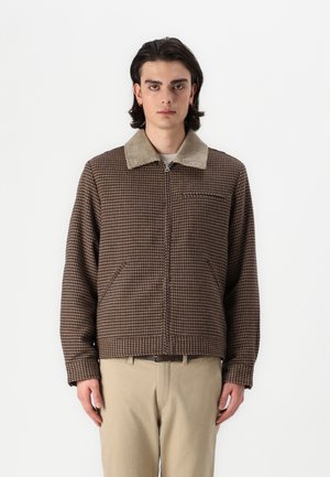 Brun rutete jakke med kordfløyelskrage, glidelås foran og sidelommer, båret over beige bukser. Ren, moderne passform.