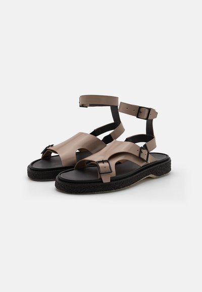 Brown rubber sandals with a wide front strap, multiple adjustable ankle straps, and a textured black sole. Buckle accents enhance secure fit.