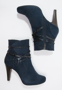 Botines de ante azul marino con punta afilada, tacón de aguja, cremalleras laterales y detalles de cadena negra alrededor del tobillo.
