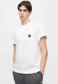 Λευκό βαμβακερό T-shirt με κοντά μανίκια, που διαθέτει μια μικρή τσέπη με γραφικά βουνών σε πράσινο και μαύρο. Κανονική εφαρμογή.