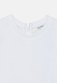 Λευκό τοπ με υφή, διαθέτει στρογγυλή λαιμόκοψη και κλείσιμο με φερμουάρ στην πλάτη. Ετικέτα ορατή στο εσωτερικό της περιοχής της λαιμόκοψης. Λείο ύφασμα.