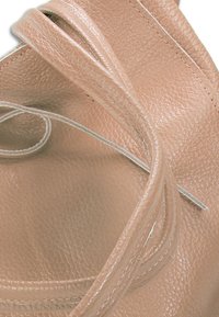 Close-up van textiel beige leer met gebogen, overlappende gestikte randen.
