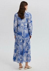 Pikk sinine kleit, millel on valged lille- ja abstraktsed mustrid, pikad varrukad ja kihiline seelikuosa. Kerge kangas ja mugav lõige.