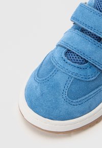 Siniset mokkanahkakengät verkkokankailla, valkoisella kumipohjalla ja säädettävillä tarranauhoilla. Kelluvat ompeleet ja pyöristetty varvasosa.