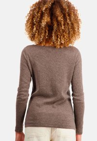 Pull marron à manches longues avec un design simple, un tissu texturé et un col arrondi, associé à un pantalon clair.