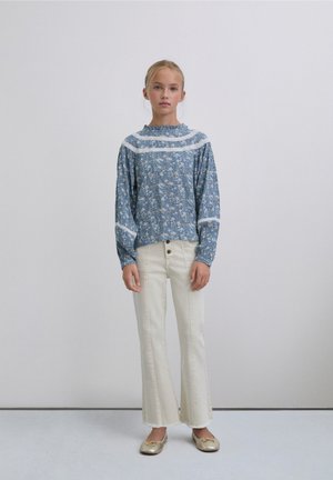 Top azul claro con estampado floral de manga larga con detalles en blanco y corte holgado, combinado con pantalones acampanados en color crema y zapatos dorados sin cordones.