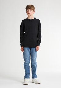 Maglione nero a maniche lunghe con scollo rotondo, abbinato a jeans di denim azzurro chiaro e sneaker bianche. Design semplice, texture morbida.