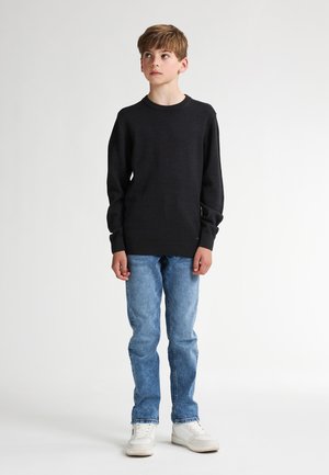 Schwarzer Langarmpullover mit Rundhalsausschnitt, kombiniert mit hellblauen Jeans und weißen Sneakers. Einfaches Design, weiche Textur.