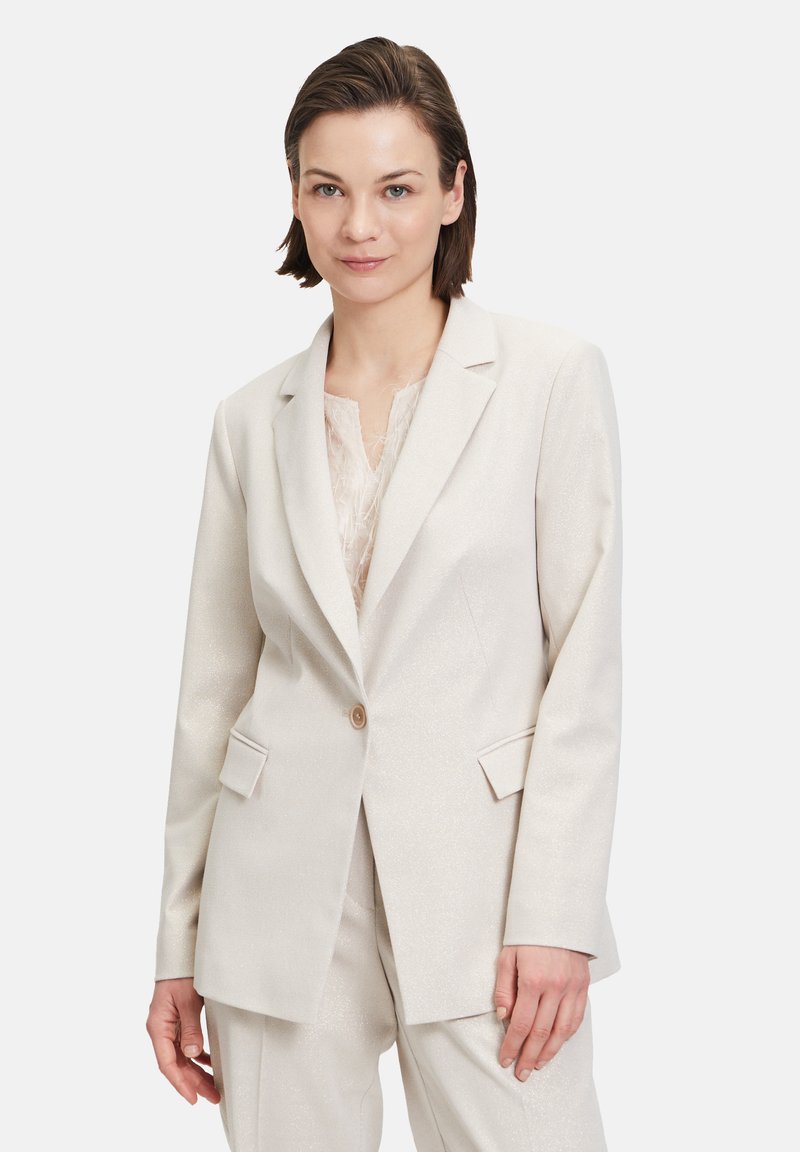 Beige blazer with a subtle shimmer, single button closure, notched lapels, and flap pockets, paired with a textured light top.