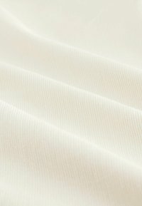 Tissu côtelé blanc présentant une texture douce avec des lignes horizontales visibles et un éclat subtil, disposé en plis délicats.