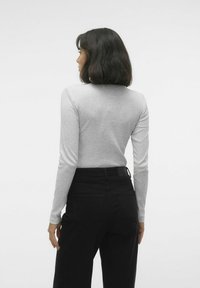Maglietta a maniche lunghe grigia chiara con un design aderente, texture liscia, abbinata a pantaloni neri a vita alta con tasche posteriori e cuciture.