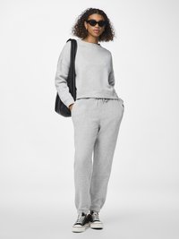 Sivý bavlnený sweatshirt a zodpovedajúce tepláky s elastickými manžetami. Model nosí čierne slnečné okuliare a tenisky. Jednoduchý, uvoľnený strih.