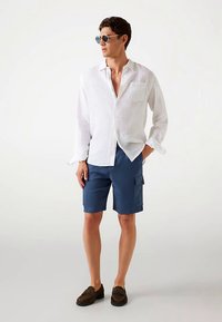 Valge linane nööbitav särk, tumesinised taskutega vööpüksid, pruunid libisemiskindlad kingad ja ümmargused päikeseprillid. Lihtne, vabaaja suve riietus.