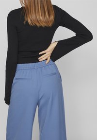 Czarny, prążkowany top z długim rękawem o dopasowanym kroju, zestawiony z jasnoniebieskimi spodniami o szerokich nogawkach z elastycznym paskiem i dwiema tylnymi kieszeniami.