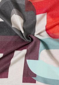 Abstract patterned fabric featuring red, gray, teal, and burgundy shapes with striped textures, displayed in a twisted arrangement.
