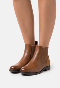 Bottines en cuir marron avec des côtés élastiques côtelés et un panneau en suede. Bout arrondi et petit talon. Texture lisse avec des accents cousus.