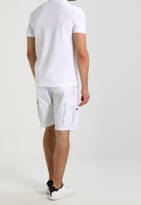 Une polo blanc associé à un short cargo, les deux en tissu léger. Le short possède plusieurs poches et un ajustement décontracté.