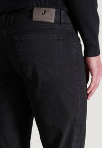 Pantalones negros de algodón con una textura suave, que cuentan con un bolsillo trasero, costuras visibles y una etiqueta de cuero en la cinturilla.
