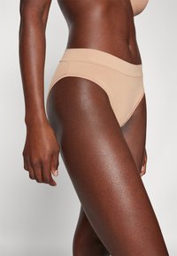 Beige high-waisted bikini briefs made from smooth fabric, showcasing a seamless design and soft elastic waistband.