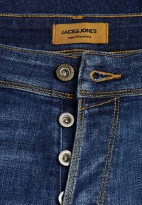 Jeans in denim di colore blu scuro con cuciture in rame, caratterizzati da un'apertura con bottone e un'etichetta beige con la scritta "JACK & JONES" e "JEANS INTELLIGENCE."