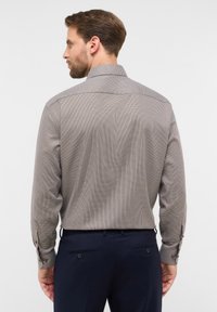 Camicia a maniche lunghe da uomo in un motivo a scacchi marrone e bianco. Presenta un colletto classico e polsini con bottoni. Tessuto strutturato.