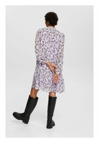 Vestido de estampado floral en lavanda transparente con mangas largas y dobladillo con volantes, combinado con altas botas de goma negras con suela gruesa.