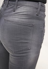 Šedé džíny z denimu s přiléhavým střihem, které mají standardní zadní kapsy, viditelné švy a hladkou strukturu.