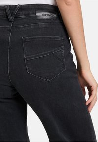 Czarne dżinsy z denimu z tylną kieszenią z wyraźnym szwem, skórzaną metką na pasku oraz dopasowanym krojem.