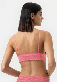 Nettobralette i lys rosa med justerbare stropper; har bølgede kanter og et blomstermønster som gir en tettsittende og teksturert design.