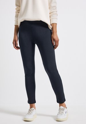 Marineblauwe stretchleggings gemaakt van een gladde stof, met een hoge tailleband en taps toelopende enkelopeningen, gecombineerd met witte sneakers.