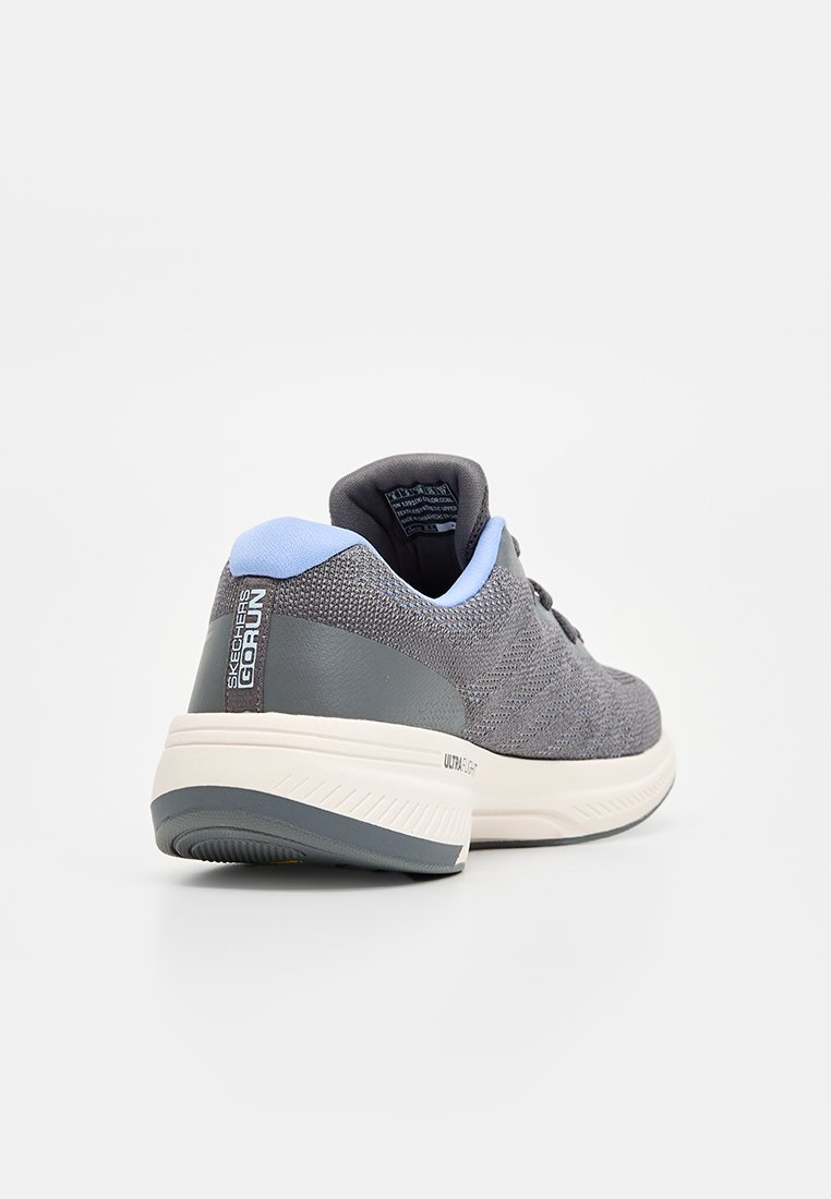 Zapatilla deportiva de punto gris con un cuello azul claro, suela acolchada y acabado texturizado. Marca visible en el talón.