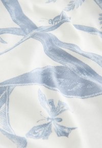 Sinine ja valge kangas, millel on botaaniline muster lehtede ja putukatega, näidates sujuvat tekstuuri ja pehmet langevust.