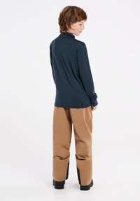 Marineblauwe langemouwen top gecombineerd met beige broek. De broek heeft zwarte accenten bij de enkels. Zachte stoftexturen zijn in beide kledingstukken zichtbaar.