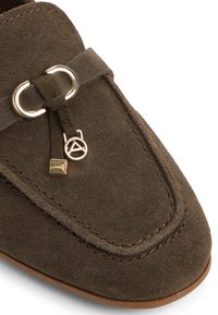 Mocassino in suede marrone con punta arrotondata, caratterizzato da un accento decorativo in hardware color oro e una suola piatta in pelle. Texture liscia e dettagli di cucitura.