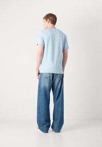 Himmelblaues, kurzärmliges T-Shirt mit glatter Textur, kombiniert mit lockeren, ausgebleichten Blue Jeams im klassischen Fünf-Taschen-Design.