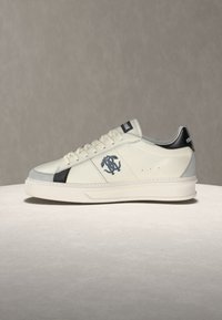 Λευκό παπούτσι χαμηλό με μαύρες και γκρι λεπτομέρειες, λογότυπο στο πλάι και χοντρή λευκή σόλα, παρουσιάζεται σε ουδέτερο φόντο.