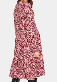 Punainen kukallinen mekko, jossa on pitkät hihat, laskostettu hame ja tekstuuriset hihansuut. Sisältää valkoisten ja vaaleanpunaisten kukkien kuviota tummalla taustalla.