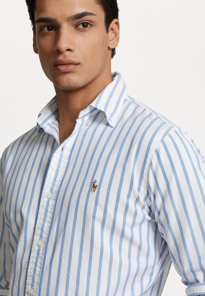 Camicia a bottoni blu e bianca a righe in cotone leggero, con un piccolo logo. Colletto classico e chiusura con bottoni. Finitura testurizzata.