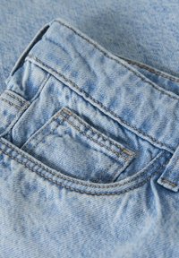 Svijetloplavi denim tkanina s ušivenim džepom i pojasom, koji prikazuje teksturiranu površinu s malo izblijedjelim izgledom.